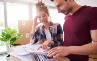 Couple reviewing moving budget with calculator and moving boxes.