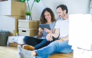 Couple moving to a new home using tablet with a happy face standing and smiling with a confident smile showing teeth