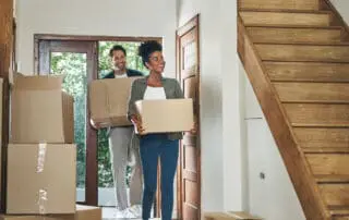 couple moving into a new modern house, carrying boxes and arriving home together. Happy, excited and smiling husband and wife walking, entering and relocating.