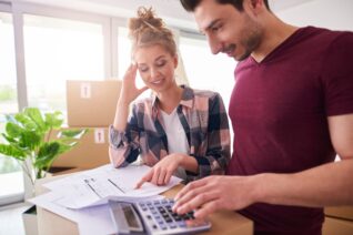 Couple reviewing moving budget with calculator and moving boxes.