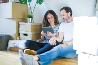 Couple moving to a new home using tablet with a happy face standing and smiling with a confident smile showing teeth