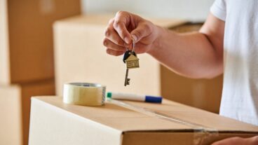 Close-up of hands holding keys symbolizing new home ownership, with blurred boxes in the background. A warm atmosphere highlighting real estate transition.