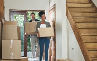 couple moving into a new modern house, carrying boxes and arriving home together. Happy, excited and smiling husband and wife walking, entering and relocating.
