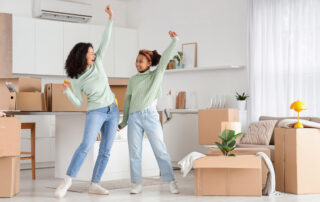 New home excitement and moving day, happy mother and daughter dancing with cardboard boxes in a modern apartment living room and kitchen area